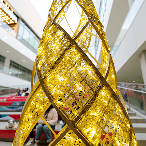 A close up of the Shinto Tree decoration is featuring a clear silicone netting that cascades over the tree in a voluminous way. Warm white mini lights are woven throughout the netting, creating a sparkling and diffused light effect. This clean and modern design gives the tree a soft, ethereal glow.