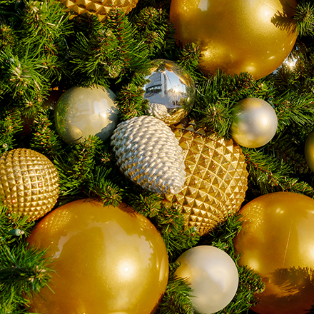 A silver pine cone ornament in a Christmas tree surrounded by other gold ornaments.